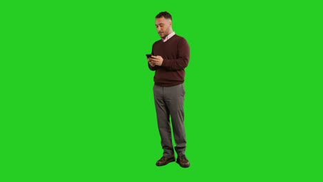 Full-Length-Studio-Portrait-Of-Mature-Male-Teacher-Or-Businessman-Standing-Against-Green-Screen-Using-Mobile-Phone-To-Message-Or-Browse-Online-2