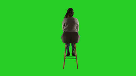 Vista-Trasera,-Fotografía-De-Estudio-De-Una-Mujer-Sentada-En-Un-Taburete-De-Espaldas-A-La-Cámara-Contra-Una-Pantalla-Verde