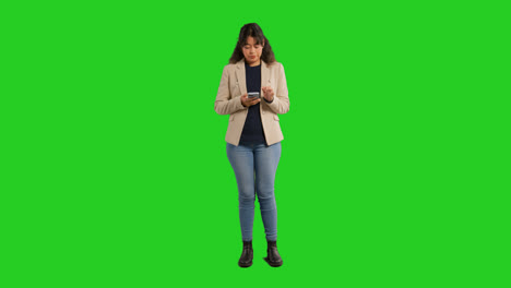 Retrato-De-Estudio-De-Cuerpo-Entero-De-Una-Profesora-O-Empresaria-Parada-Frente-A-Una-Pantalla-Verde-Usando-Un-Teléfono-Móvil-Para-Enviar-Mensajes-O-Navegar-En-Línea.