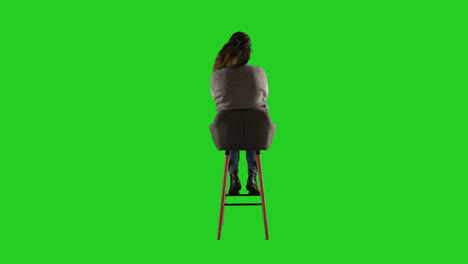 Vista-Trasera,-Fotografía-De-Estudio-De-Una-Mujer-Sentada-En-Un-Taburete-De-Espaldas-A-La-Cámara-Contra-Una-Pantalla-Verde