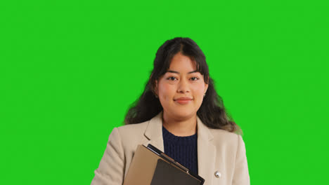 Close-Up-Studio-Portrait-Of-Female-Teacher-Or-Businesswoman-Standing-Against-Green-Screen-Carrying-Folder