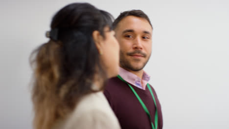 Male-And-Female-Teachers-Wearing-Security-Lanyards-Talking-As-They-Walk-Past-Camera-Against-White-Background