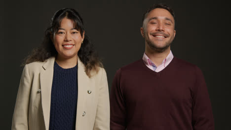 Retrato-De-Estudio-De-Profesores-Hombres-Y-Mujeres-Sonrientes-Caminando-Hacia-La-Cámara-Y-De-Pie-Contra-Un-Fondo-Negro.