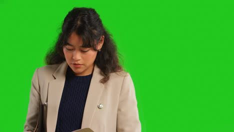 Close-Up-Studio-Shot-Of-Female-Teacher-Or-Businesswoman-Reading-Notebook-Against-Green-Screen-Background