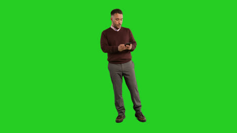 Full-Length-Studio-Portrait-Of-Mature-Male-Teacher-Or-Businessman-Standing-Against-Green-Screen-Using-Mobile-Phone-To-Message-Or-Browse-Online-1