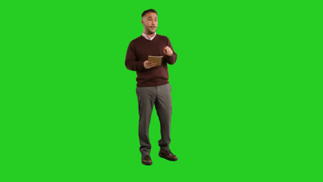 Full-Length-Studio-Portrait-Of-Mature-Male-Teacher-With-Notebook-Talking-To-Class-Standing-Against-Green-Screen