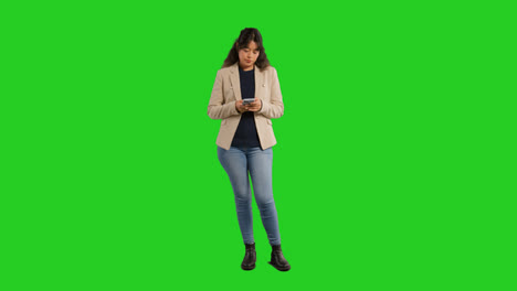 Full-Length-Studio-Portrait-Of-Female-Teacher-Or-Businesswoman-Standing-Against-Green-Screen-Using-Mobile-Phone-To-Message-Or-Browse-Online-1