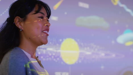 Female-Teacher-Giving-Astronomy-Lesson-In-School-Standing-At-The-Front-Of-Class-With-Projection-Of-The-Solar-System-3