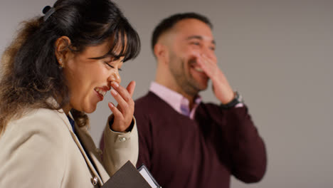 Nahaufnahme-Einer-Studioaufnahme-Von-Männlichen-Und-Weiblichen-Lehrern-Vor-Grauem-Hintergrund,-Die-Zusammen-Lachen-Und-Lächeln