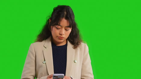 Close-Up-Studio-Shot-Of-Businesswoman-Using-Mobile-Phone-To-Message-Or-Browse-Online-Standing-Against-Green-Screen