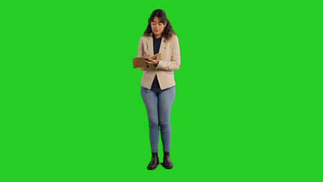 Full-Length-Studio-Portrait-Of-Female-Teacher-With-Notebook-Talking-To-Class-Standing-Against-Green-Screen