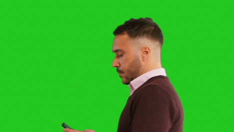 Close-Up-Studio-Shot-Of-Walking-Businessman-Using-Mobile-Phone-To-Message-Or-Browse-Online-Standing-Against-Green-Screen-1