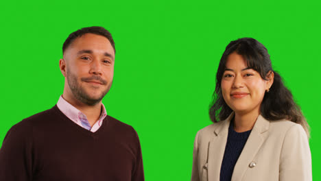 Close-Up-Studio-Portrait-Of-Smiling-Male-And-Female-Teachers-Or-Businesspeople-Talking-Before-Looking-At-Camera-Against-Green-Screen