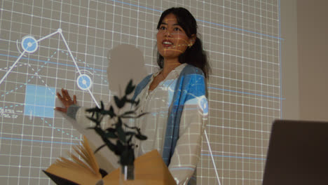 Female-Teacher-Giving-Maths-Or-Science-Lesson-In-School-Standing-At-The-Front-Of-Class-With-Projection-Of-Graph