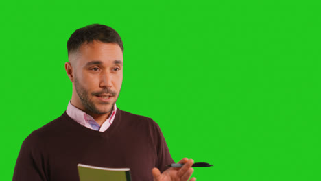 Close-Up-Studio-Portrait-Of-Mature-Male-Teacher-Talking-To-Class-Standing-Against-Green-Screen-Background