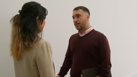 Male-And-Female-Teachers-Meeting-And-Talking-As-They-Walk-Along-Corridor-In-School-Building-2