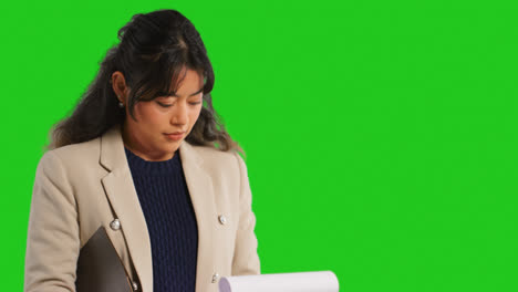 Close-Up-Studio-Portrait-Of-Female-Teacher-Or-Businesswoman-Standing-Against-Green-Screen-Looking-At-Clipboard-1