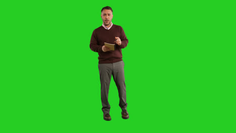 Full-Length-Studio-Portrait-Of-Mature-Male-Teacher-With-Notebook-Talking-To-Class-Standing-Against-Green-Screen-1