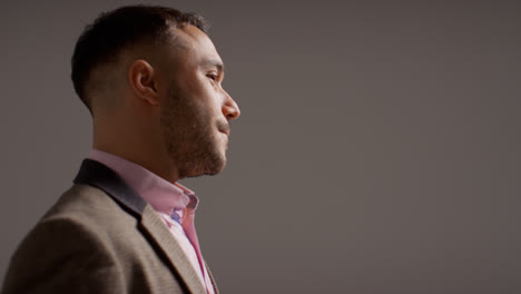 Side-View-Studio-Portrait-Of-Smiling-Mature-Male-Teacher-Wearing-Jacket-Standing-Against-Grey-Background-Shot-In-Slow-Motion