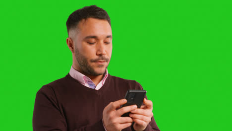 Close-Up-Studio-Shot-Of-Businessman-Using-Mobile-Phone-To-Message-Or-Browse-Online-Standing-Against-Green-Screen