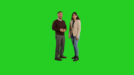 Full-Length-Studio-Portrait-Of-Male-And-Female-Teachers-Or-Businesspeople-Talking-And-Looking-At-Camera-Against-Green-Screen