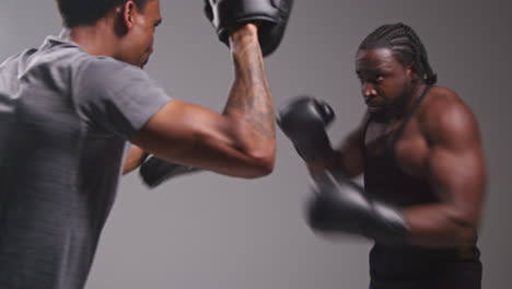 Studioaufnahme-Eines-Männlichen-Boxers-Beim-Sparring-Mit-Einem-Trainer,-Der-Schlagpolster-Oder-Handschuhe-Trägt-Und-Für-Den-Kampf-übt-4