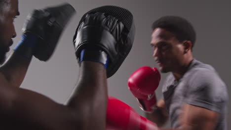 Studioaufnahme-Eines-Männlichen-Boxers-Beim-Sparring-Mit-Einem-Trainer,-Der-Schlagpolster-Oder-Handschuhe-Trägt-Und-Für-Den-Kampf-übt-7