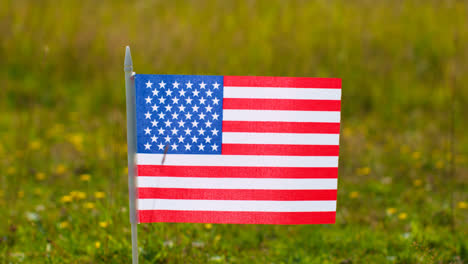 Close-Up-Of-Small-American-Stars-And-Stripes-Flag-Outdoors-In-Countryside-Field-Or-Garden-Moving-In-Wind