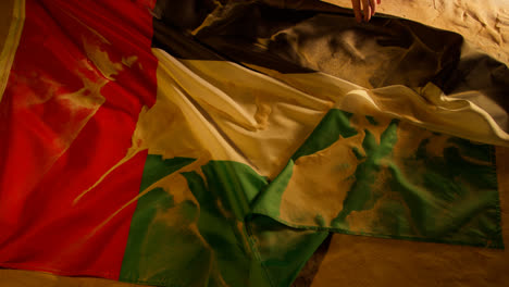 Overhead-Studio-Shot-Showing-Person-Unfolding-National-Flag-Of-UAE-United-Arab-Emirates-On-Sandy-Desert-Background-1