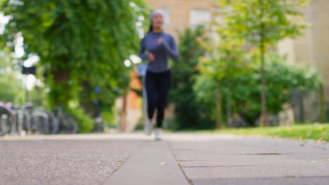 Toma-A-Nivel-Del-Suelo-De-Una-Mujer-Joven-Haciendo-Ejercicio-Corriendo-Hacia-La-Cámara-En-Foco-En-Un-Parque-De-La-Ciudad