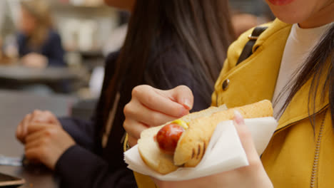 Close-Up-Of-Two-Women-Buying-Hot-Dogs-From-Street-Food-Market-Stall