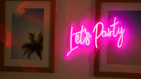 Close-Up-Of-Neon-Let's-Party-Sign-Hanging-On-Wall-At-House-Party