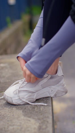 Vídeo-Vertical-De-Cerca-De-Una-Mujer-Atándose-Los-Cordones-De-Una-Zapatilla-Deportiva-Antes-De-Hacer-Ejercicio-Corriendo-Por-Una-Calle-Urbana