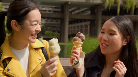 Dos-Amigas-Jóvenes-Sonrientes-Se-Encuentran-Y-Comen-Helado-Al-Aire-Libre-En-El-Parque-Juntas-2