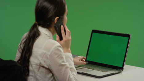 Businesswoman-working-on-laptop-answers-phone-on-green-screen