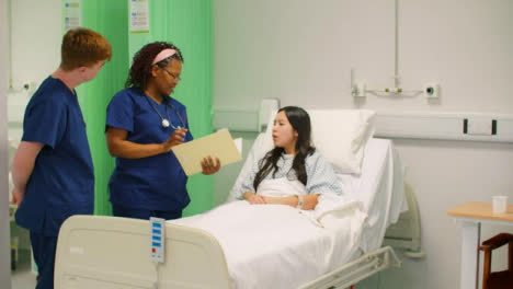 Two-Nurses-Talk-To-Patient-in-Hospital-Bed