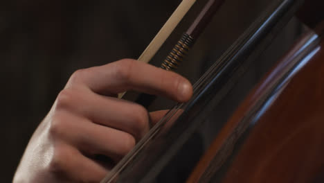 Vista-lateral-cerca-de-violonchelista-masculino-tocando-cuerdas-en-violonchelo