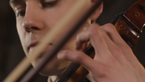 Pan-abajo-cerca-de-violonchelista-masculino-tocando-cuerdas-en-violonchelo