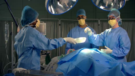Asistente-de-sexo-femenino-que-pasa-el-instrumento-quirúrgico-al-cirujano