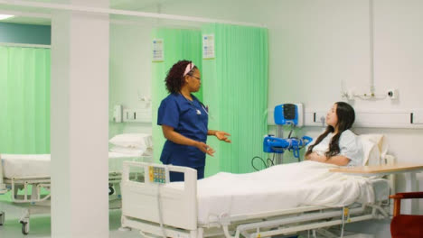 Female-Nurse-Chatting-to-Patient-in-Hospital-Bed