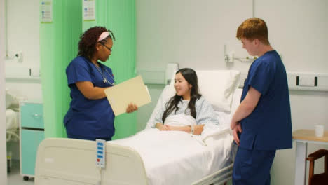 Zwei-Krankenschwestern-Mit-Akte-Sprechen-Mit-Patient-Im-Krankenhausbett