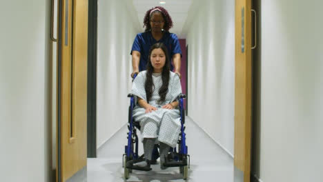 Krankenschwester-Schiebt-Patienten-Im-Rollstuhl-In-Den-Flur