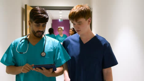 médico-Staff-Using-Tablet-Walking-In-Corridor