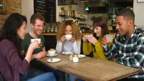 A-Group-Of-Friends-Chatting-And-Drinking-Coffee-At-Table-In-Cafe