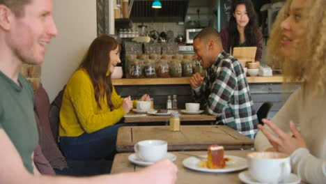 Dos-parejas-hablando-en-mesas-en-café