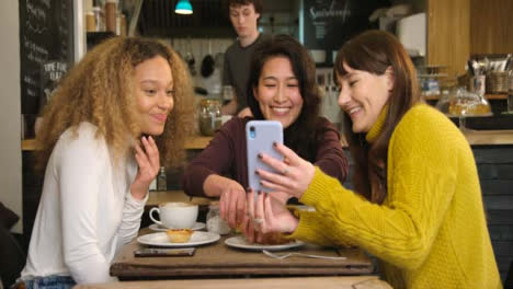 Una-mujer-muestra-a-sus-amigos-algo-divertido-por-teléfono-en-el-café