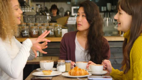 Panning-Across-three-friends-socialising-around-table-in-cafe