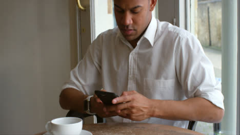 Incline-al-cliente-masculino-sentado-en-la-cafetería-con-teléfono-inteligente
