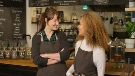 Two-happy-female-baristas-at-a-cafe-smiling-at-each-other