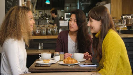 Group-Of-Female-Friends-Chatting-And-Laughing-At-Table-In-Cafe